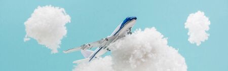 toy plane flying among white fluffy clouds made of cotton wool isolated on blue, panoramic shot