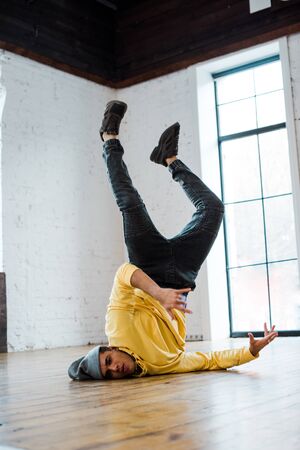 handsome man in hat breakdancing on floor in dance studio