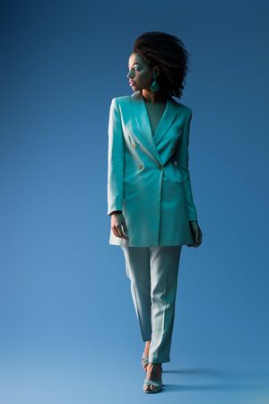 attractive african american woman in suit looking away on blue backgroundの写真素材