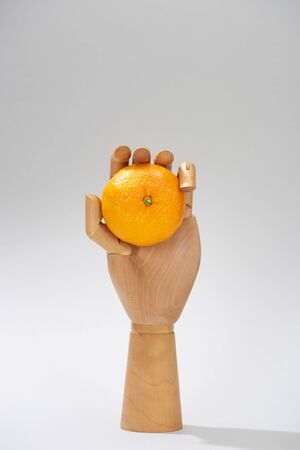 Wooden hand of doll with fresh mandarin on grey backgroundの写真素材
