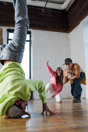 selective focus of emotional dancers looking at african american man breakdancing in dance studioの写真素材