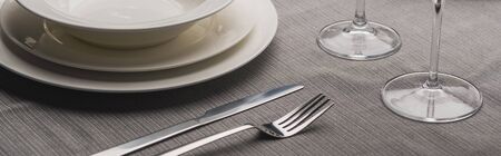 Serving plates with cutlery and wine glasses on grey cloth, panoramic shotの写真素材