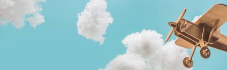 wooden toy plane flying among white fluffy clouds made of cotton wool isolated on blue, panoramic shotの写真素材