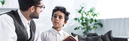 panoramic shot of jewish father and son talking and holding tanakh in apartmentの写真素材