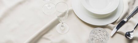 High angle view of dinnerware with cutlery and glasses on white tablecloth, panoramic shotの写真素材