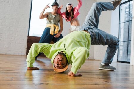 selective focus of african american man breakdancing near emotional dancers