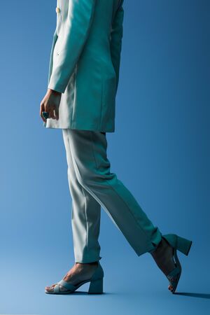 cropped view of african american woman in suit walking on blue backgroundの写真素材