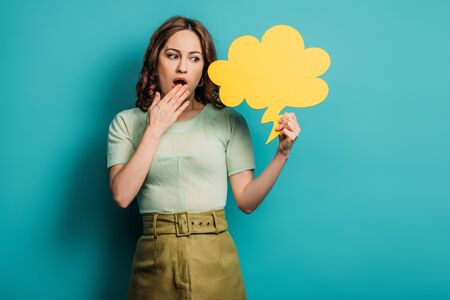 shocked woman holding hand near mouth while holding thought bubble on blue background