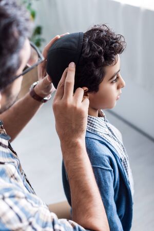 cropped view of jewish father wearing hat on son in apartmentの写真素材