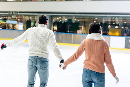 back view of young couple holding hands on skating rink の写真素材