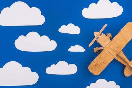 top view of wooden toy plane in blue sky with paper cut white cloudsの写真素材