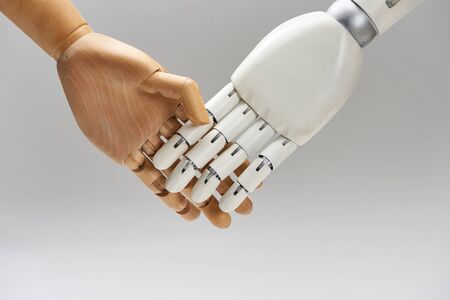 Wooden doll and robot handshaking isolated on greyの写真素材