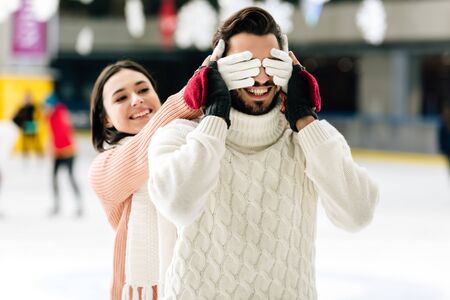 happy girl closing eyes to smiling man to make a surprise on skating rinkの写真素材