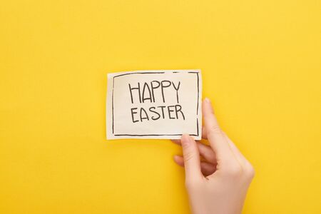 cropped view of woman holding greeting card with happy Easter lettering on yellow backgroundの写真素材