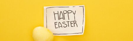 top view of greeting card with happy Easter lettering and painted egg on yellow colorful background, panoramic shotの写真素材