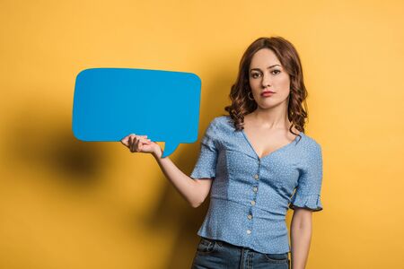 offended girl looking at camera while holding speech bubble on yellow background