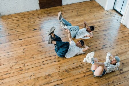 overhead view of trendy girl lying on floor with multicultural dancers while breakdancing in dance studioの写真素材