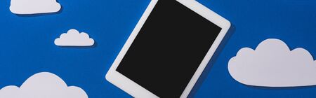 top view of white paper cut clouds and digital tablet on blue background, panoramic shot