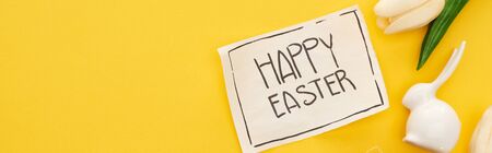 top view of tulips, greeting card with happy Easter lettering, easter bunny on yellow colorful...