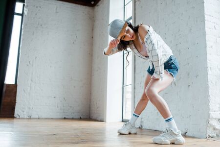 attractive girl touching cap while dancing hip-hopの写真素材