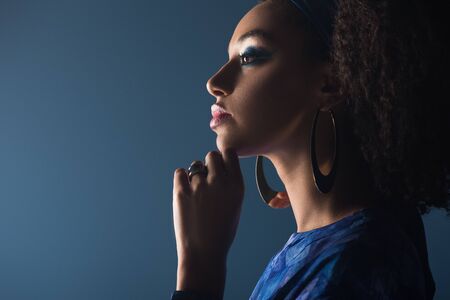 side view of attractive african american woman with accessories isolated on blue