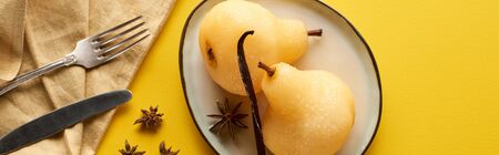 top view of delicious pear in wine with anise on plate near cutlery and napkin on yellow background, panoramic shotの写真素材