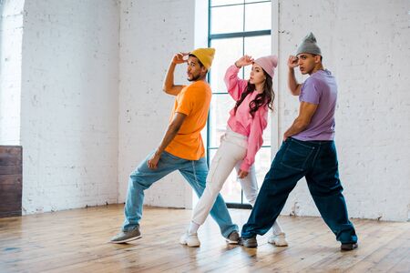 multicultural dancers touching hats while breakdancing in dance studio