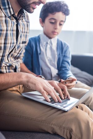 cropped view of jewish father using laptop and son holding credit card in apartmentの写真素材