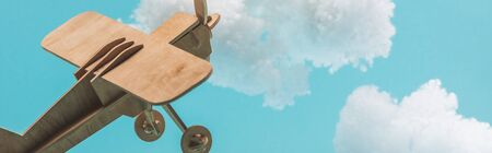 wooden toy plane flying among white fluffy clouds made of cotton wool isolated on blue, panoramic shotの写真素材