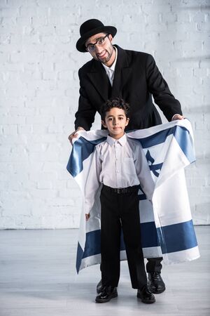 smiling jewish father holding flag of israel and cute son looking at cameraの写真素材