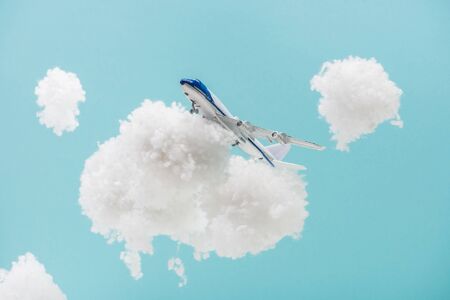 toy plane flying among white fluffy clouds made of cotton wool isolated on blueの写真素材