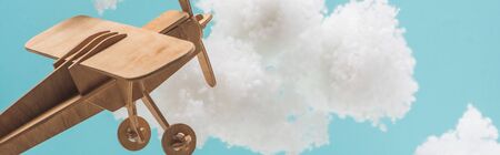 wooden toy plane flying among white fluffy clouds made of cotton wool isolated on blue, panoramic...