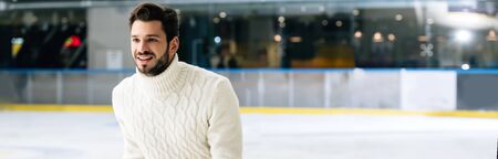 panoramic shot of handsome smiling man in jeans and sweater skating on rinkの写真素材
