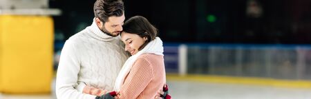 panoramic shot of beautiful young couple in sweaters hugging on skating rink