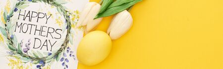 top view of spring tulips, Easter egg and happy mothers day greeting card on colorful yellow...