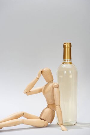 Wooden doll with hand by head beside wine bottle on grey backgroundの写真素材