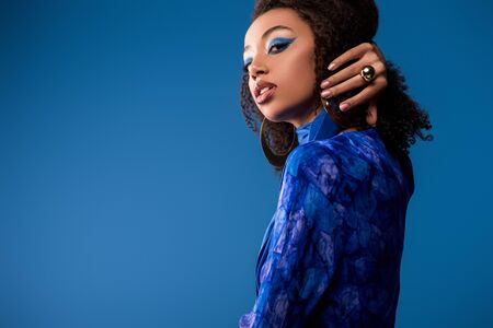 attractive african american woman in stylish dress looking at camera isolated on blueの写真素材