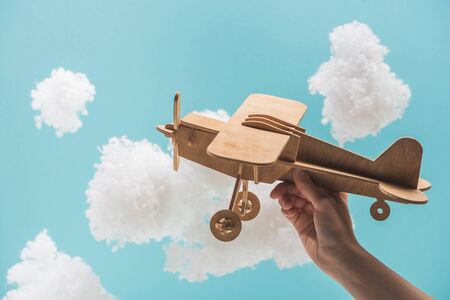 wooden toy plane flying among white fluffy clouds made of cotton wool isolated on blueの写真素材