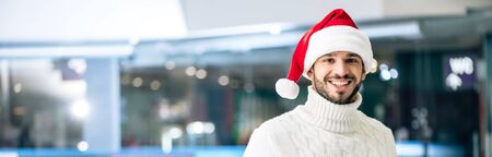panoramic shot of handsome cheerful man in sweater and santa hat on skating rinkの写真素材