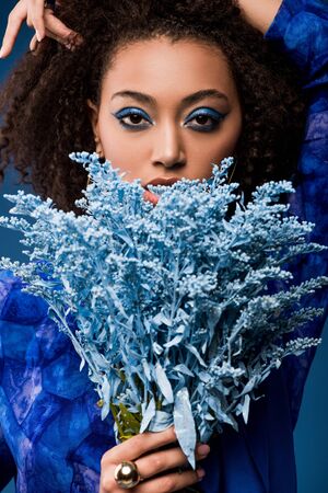 african american woman with makeup holding bouquet isolated on blueの写真素材