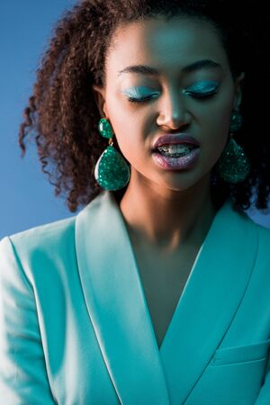 stylish african american woman with closed eyes and braces isolated on blueの写真素材