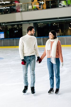 beautiful smiling couple holding hands on skating rinkの写真素材