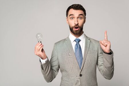 excited businessman holding light bulb and showing idea sign isolated on greyの写真素材