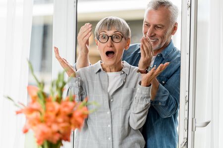 selective focus of smiling man and shocked woman looking at bouquet in new houseの写真素材