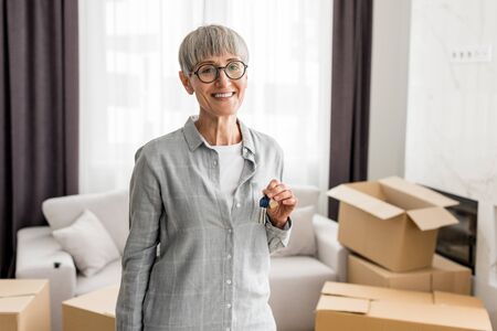 smiling woman holding keys and looking at camera in new house