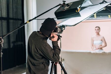 Selective focus of cameraman working with beautiful model in photo studio