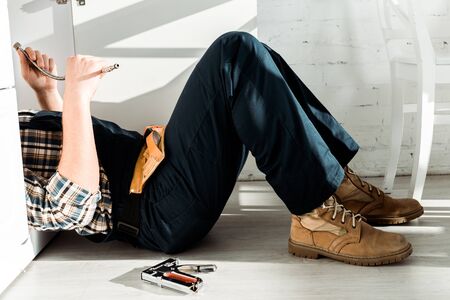 cropped view of installer lying on floor near kitchen cabinetの写真素材