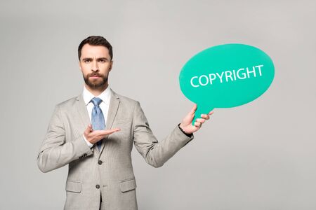 confident businessman pointing with hand at thought bubble with copyright inscription isolated on greyの写真素材