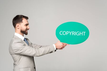 side view of smiling businessman holding thought bubble with copyright inscription isolated on greyの写真素材