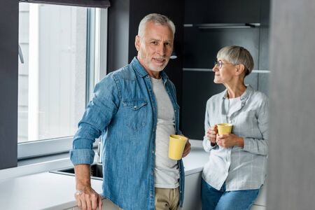 smiling man and mature woman holding cups in new houseの写真素材
